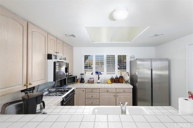 kitchen featuring stainless steel appliances, light brown cabinets, and tile counters