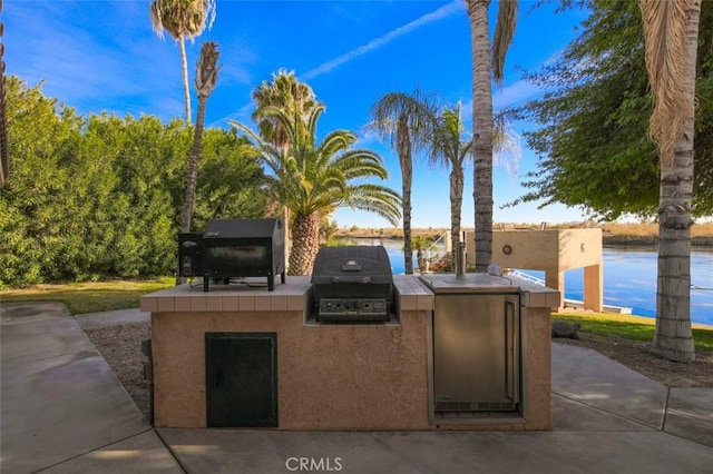 view of patio / terrace featuring a grill, a water view, and exterior kitchen