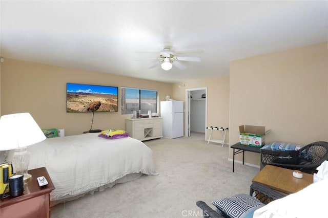 carpeted bedroom with ceiling fan, white refrigerator, a closet, and a walk in closet