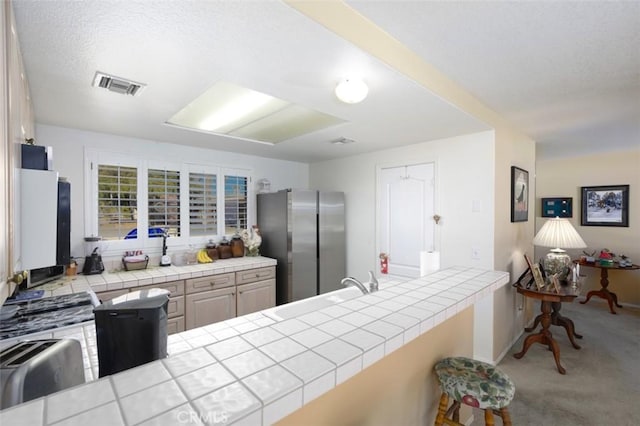 kitchen featuring kitchen peninsula, tile counters, light colored carpet, stainless steel refrigerator, and sink