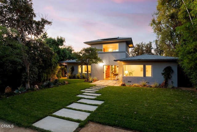 back house at dusk featuring a lawn and solar panels