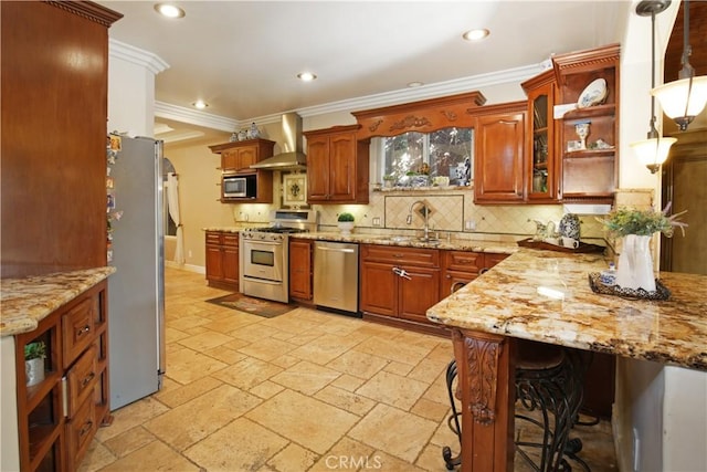 kitchen with light stone countertops, pendant lighting, appliances with stainless steel finishes, wall chimney exhaust hood, and crown molding