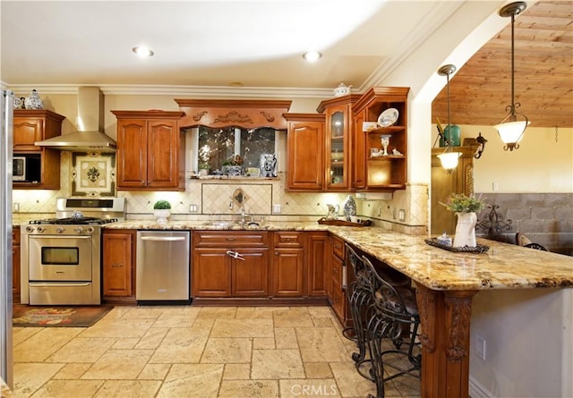 kitchen featuring pendant lighting, a breakfast bar, light stone countertops, stainless steel appliances, and wall chimney exhaust hood