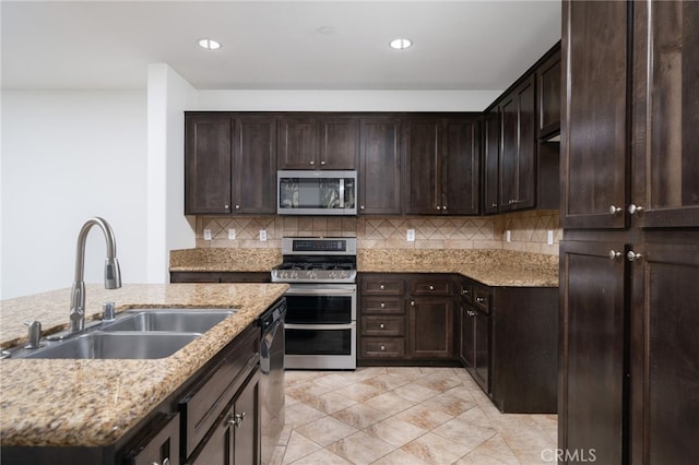 kitchen with sink, dark brown cabinetry, appliances with stainless steel finishes, an island with sink, and light stone counters