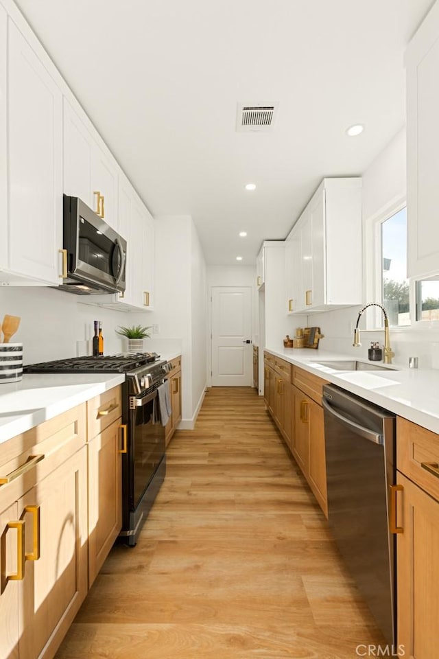 kitchen with white cabinets, appliances with stainless steel finishes, sink, and light hardwood / wood-style flooring