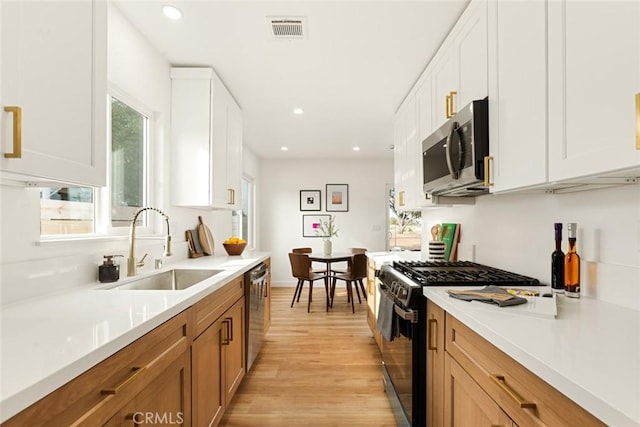 kitchen with light wood-type flooring, stainless steel appliances, white cabinets, and sink