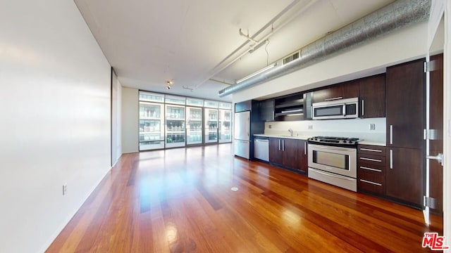 kitchen with hardwood / wood-style floors, dark brown cabinetry, stainless steel appliances, sink, and expansive windows