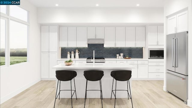 kitchen featuring white cabinetry, stainless steel appliances, an island with sink, sink, and a kitchen breakfast bar