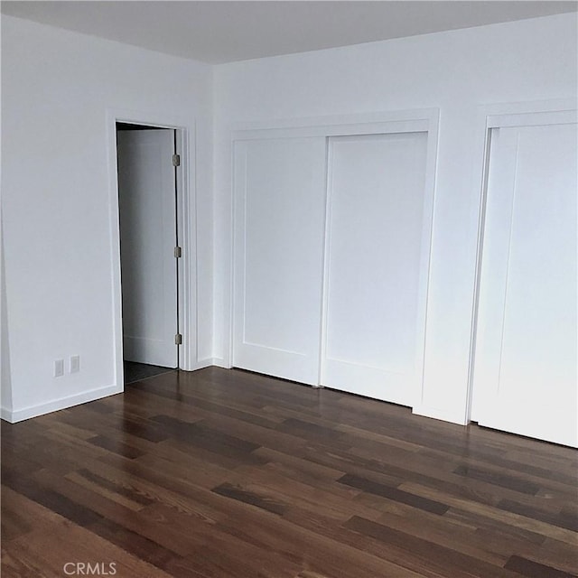 unfurnished bedroom with baseboards, multiple closets, and dark wood-style flooring