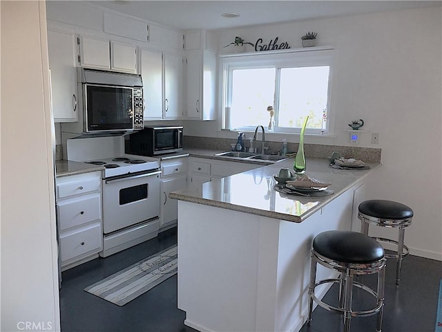 kitchen featuring white range with electric stovetop, sink, white cabinetry, and a breakfast bar area