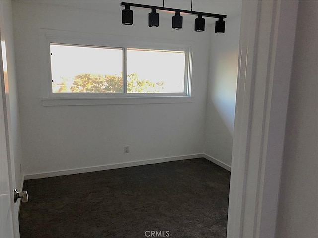 spare room with baseboards and dark colored carpet