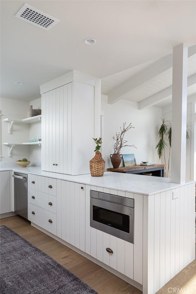 bar with white cabinetry, beam ceiling, built in microwave, stainless steel dishwasher, and light hardwood / wood-style flooring