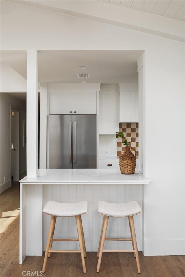 kitchen featuring kitchen peninsula, white cabinets, a kitchen bar, and stainless steel built in refrigerator