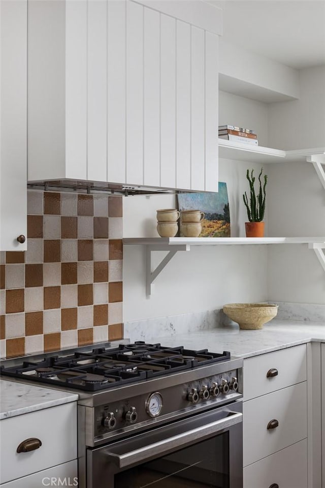 kitchen with stainless steel range, light stone countertops, decorative backsplash, and white cabinetry