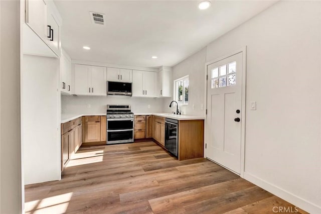 kitchen featuring sink, white cabinetry, appliances with stainless steel finishes, light hardwood / wood-style floors, and backsplash