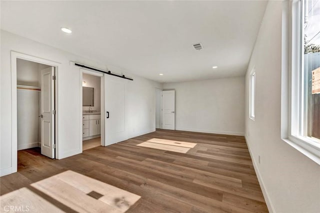 unfurnished bedroom with ensuite bath, wood-type flooring, a barn door, a walk in closet, and a closet