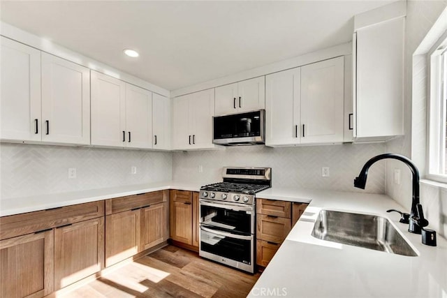 kitchen featuring sink, appliances with stainless steel finishes, backsplash, light hardwood / wood-style floors, and white cabinets