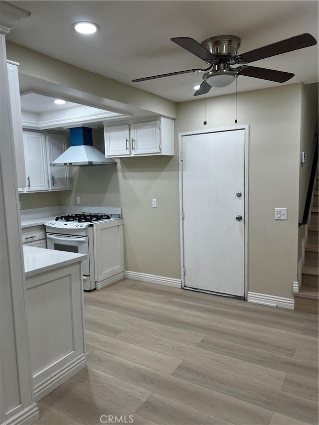 kitchen with light wood finished floors, light countertops, white cabinets, white range with gas stovetop, and wall chimney exhaust hood