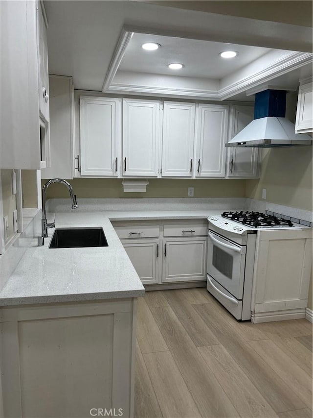 kitchen featuring white cabinets, wall chimney exhaust hood, white gas stove, light wood-style floors, and a sink