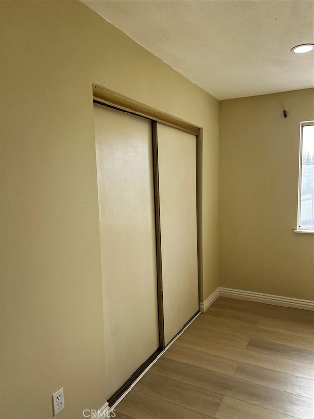 unfurnished bedroom featuring a textured ceiling, a closet, light wood-type flooring, and baseboards