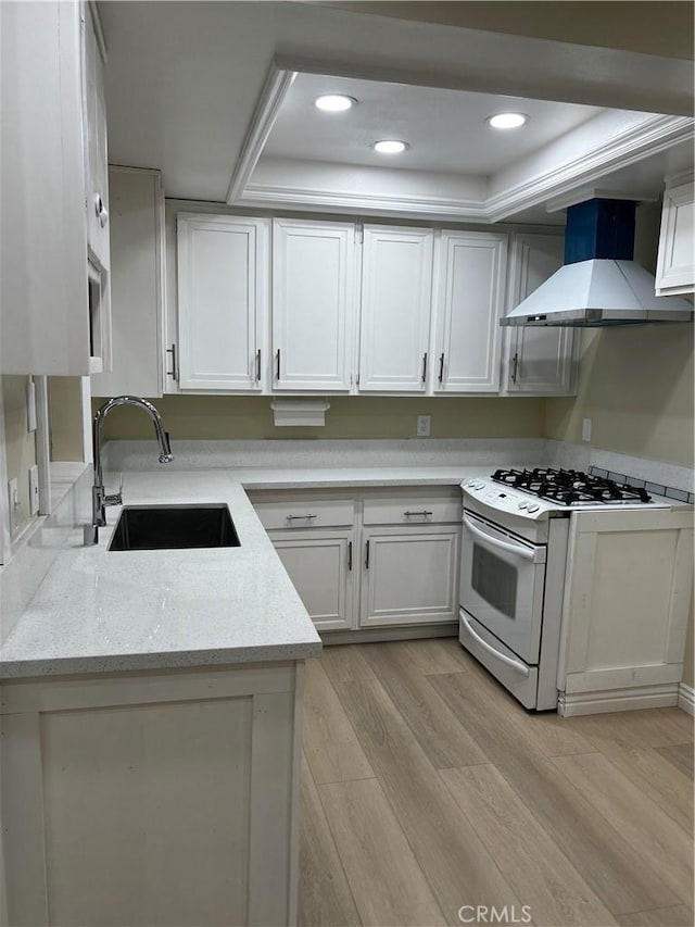 kitchen featuring a sink, white range with gas cooktop, white cabinets, light wood-type flooring, and wall chimney exhaust hood