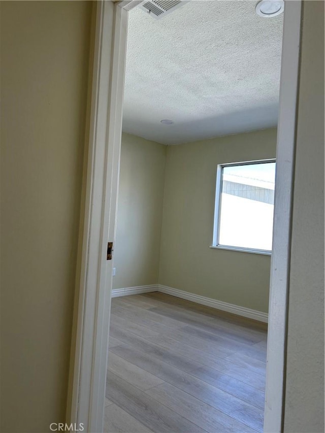 unfurnished room featuring visible vents, baseboards, a textured ceiling, and light wood finished floors