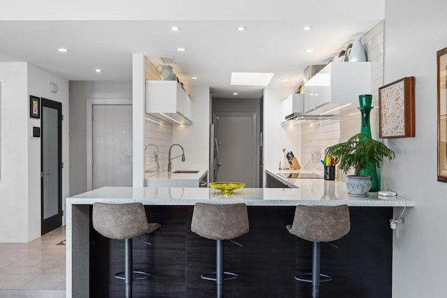 kitchen with white cabinets, a skylight, sink, kitchen peninsula, and a breakfast bar