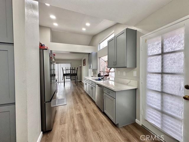 kitchen with appliances with stainless steel finishes, light hardwood / wood-style floors, sink, gray cabinets, and vaulted ceiling