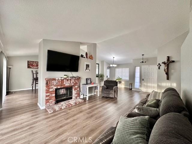 living room featuring vaulted ceiling, an inviting chandelier, hardwood / wood-style flooring, and a brick fireplace