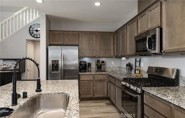 kitchen featuring light stone counters, sink, appliances with stainless steel finishes, and light wood-type flooring