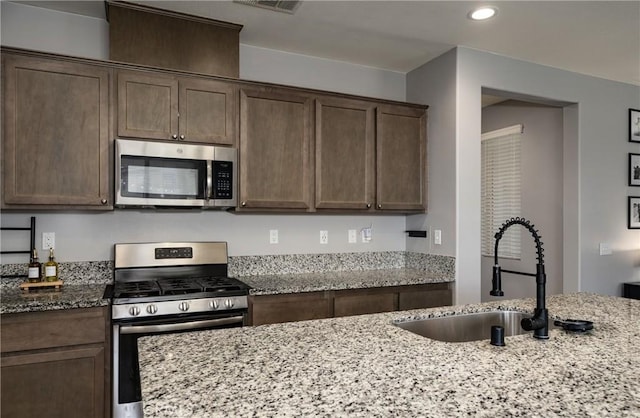 kitchen with appliances with stainless steel finishes, sink, light stone counters, and dark brown cabinetry