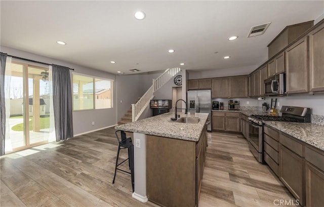 kitchen featuring a breakfast bar, sink, light stone countertops, an island with sink, and stainless steel appliances