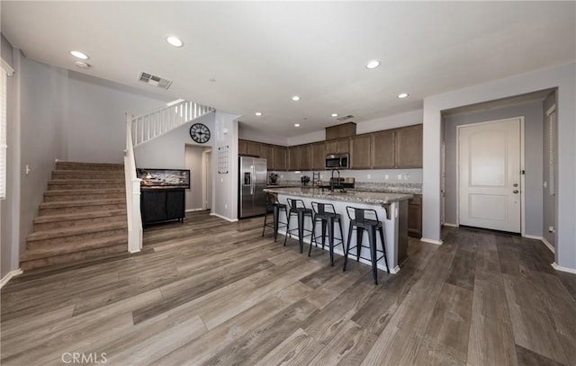 kitchen featuring dark hardwood / wood-style flooring, stainless steel appliances, a kitchen breakfast bar, light stone counters, and a center island with sink