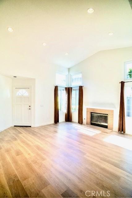 unfurnished living room with vaulted ceiling, a brick fireplace, and light wood-type flooring