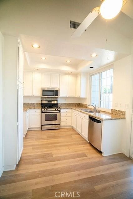 kitchen featuring sink, light hardwood / wood-style flooring, light stone countertops, appliances with stainless steel finishes, and white cabinets