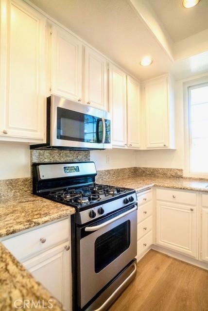 kitchen featuring white cabinets, light stone countertops, stainless steel appliances, and light hardwood / wood-style floors