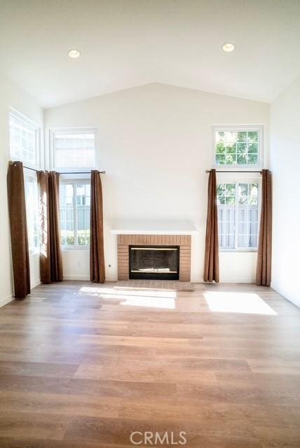 unfurnished living room with vaulted ceiling, a fireplace, and light hardwood / wood-style flooring