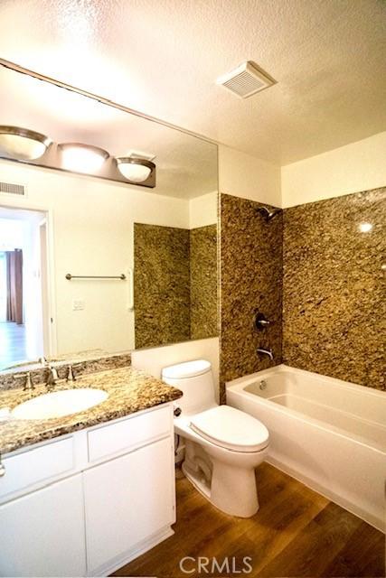 full bathroom featuring hardwood / wood-style floors, tiled shower / bath combo, a textured ceiling, vanity, and toilet