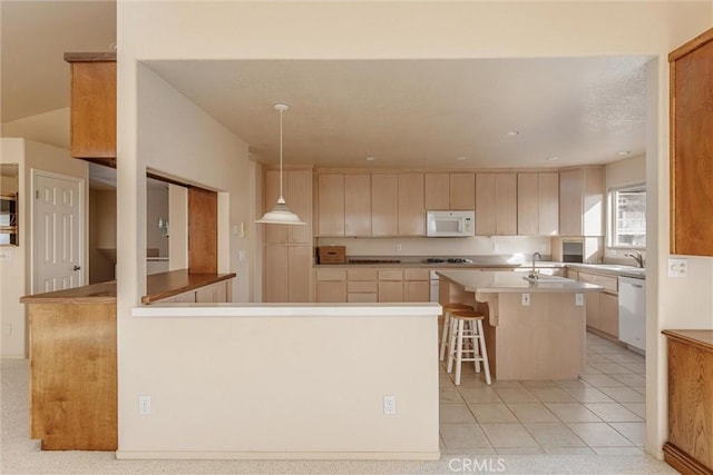 kitchen with light brown cabinets, decorative light fixtures, a kitchen island with sink, dishwasher, and a breakfast bar