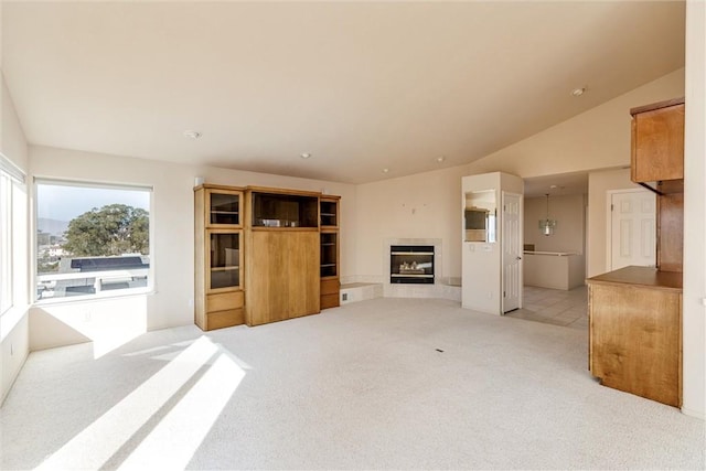 unfurnished living room featuring light carpet, a healthy amount of sunlight, and lofted ceiling