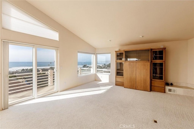 unfurnished living room featuring a beach view, light colored carpet, lofted ceiling, and a water view