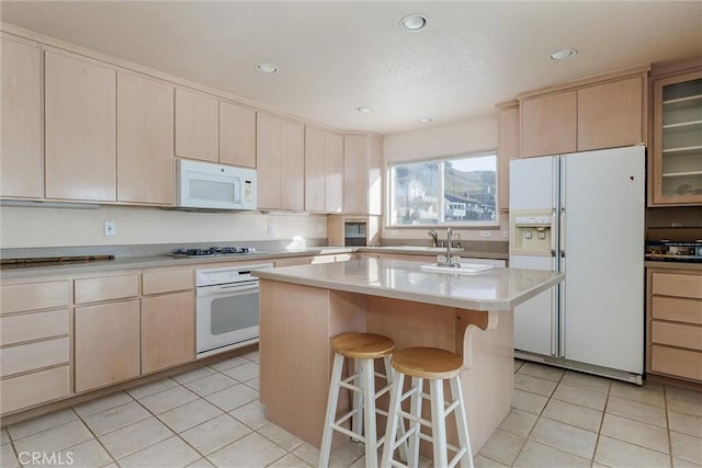 kitchen with white appliances, a center island, sink, light tile patterned flooring, and a breakfast bar