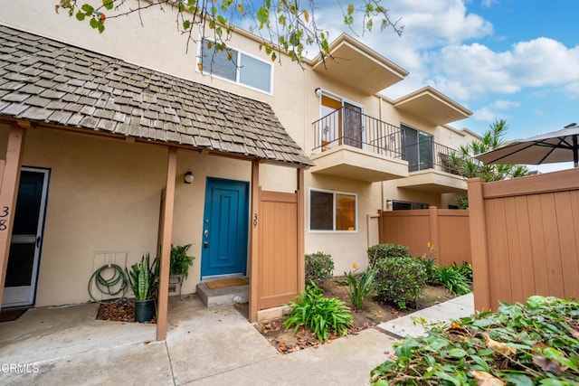 doorway to property featuring a balcony, stucco siding, and fence