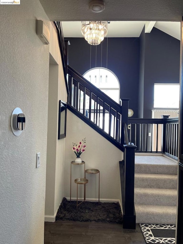 stairway with a towering ceiling, a wealth of natural light, an inviting chandelier, and hardwood / wood-style flooring