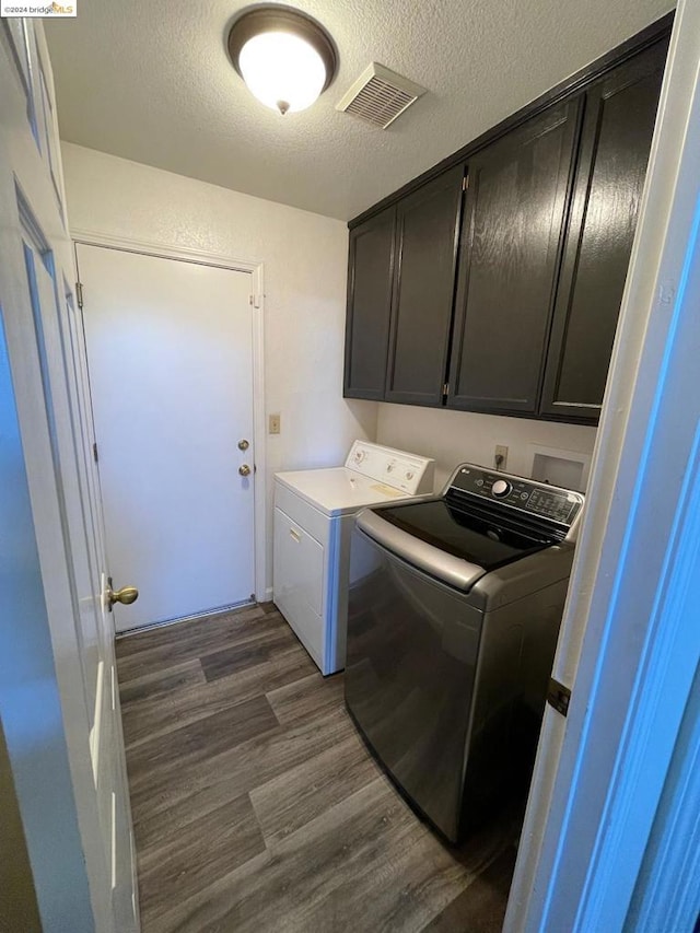 laundry area with a textured ceiling, dark wood-type flooring, washing machine and clothes dryer, and cabinets