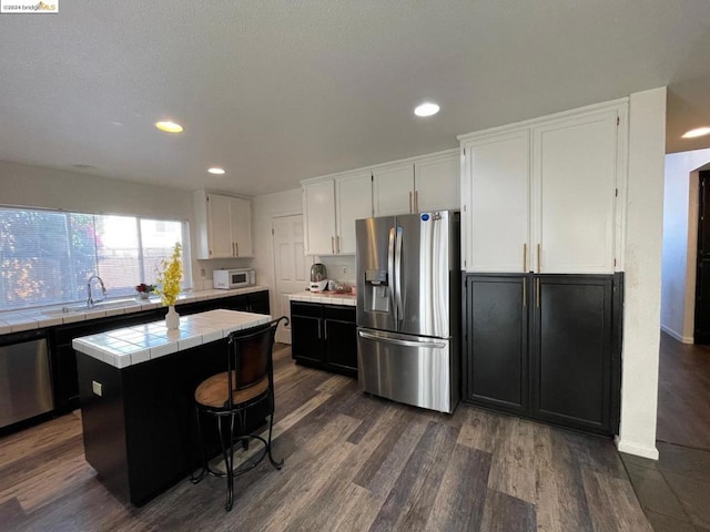 kitchen with stainless steel appliances, tile counters, a center island, white cabinets, and sink