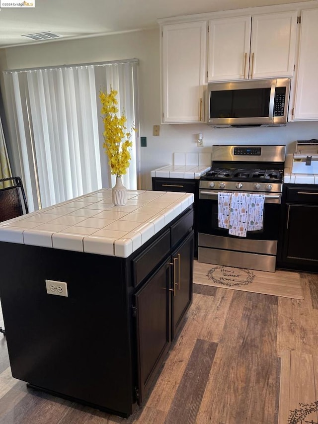 kitchen featuring light wood-type flooring, appliances with stainless steel finishes, white cabinets, and tile counters