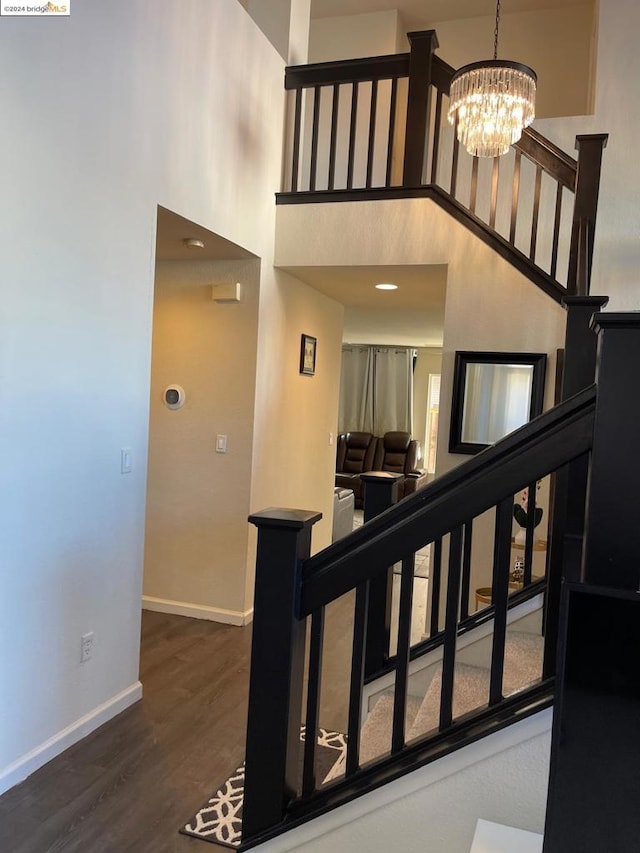 stairway featuring a towering ceiling, wood-type flooring, and a notable chandelier