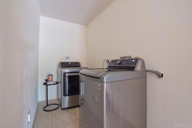 clothes washing area featuring light tile patterned floors, washing machine and dryer, and a textured ceiling