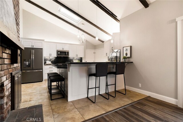 kitchen featuring appliances with stainless steel finishes, a breakfast bar, white cabinets, backsplash, and kitchen peninsula